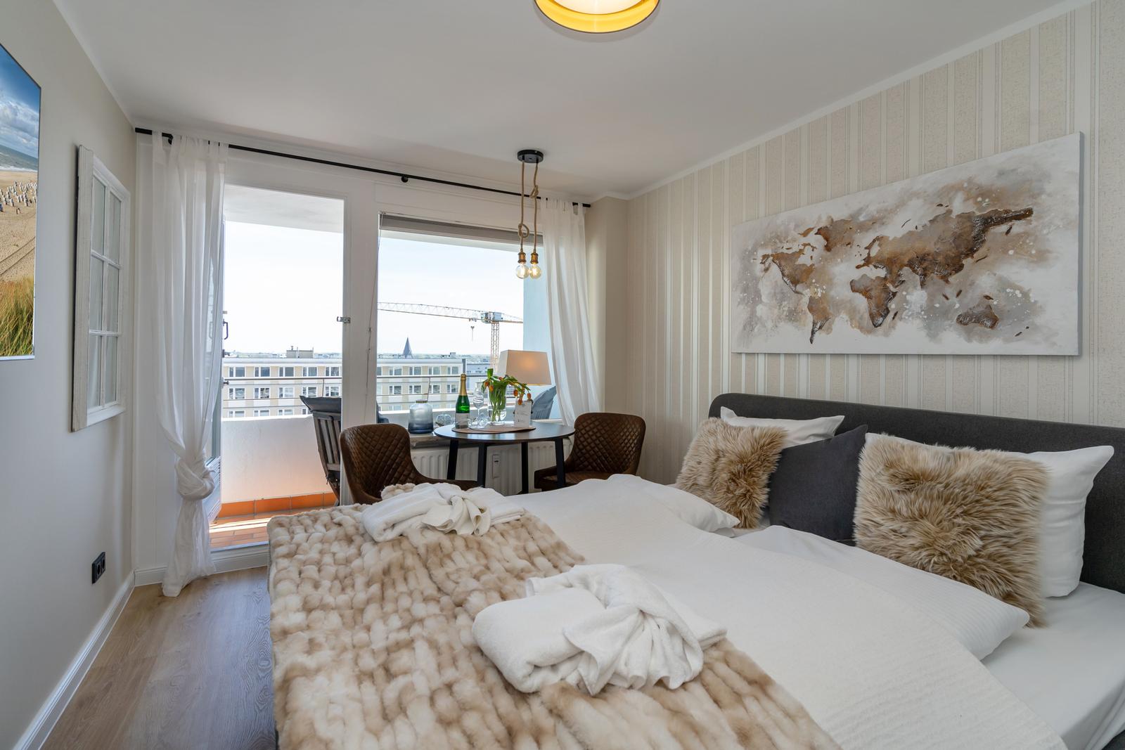 Schlafzimmer mit Balkon, Bett, Kissen und Weltkarte an der Wand.