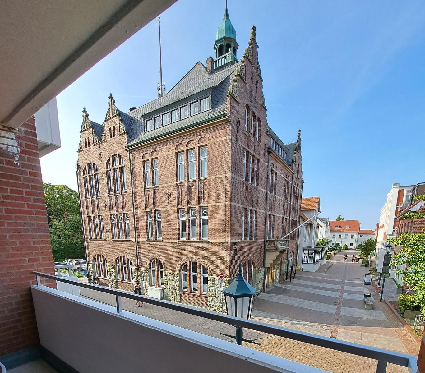 Blick von Balkon auf historisches Backsteingebäude mit Turm und gepflasterten Straße.