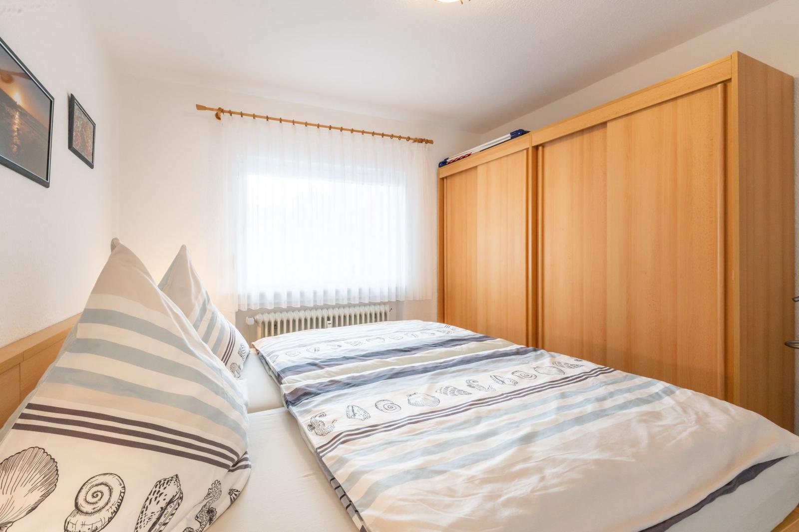 Schlafzimmer mit Bett, Schrank und Fenster mit Vorhängen.