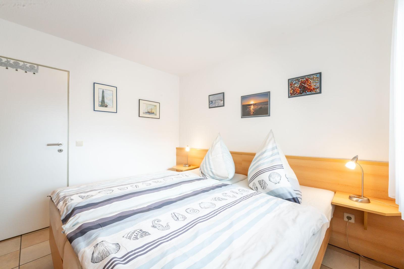 Schlafzimmer mit Bett, Nachttischen und Wandbildern.
