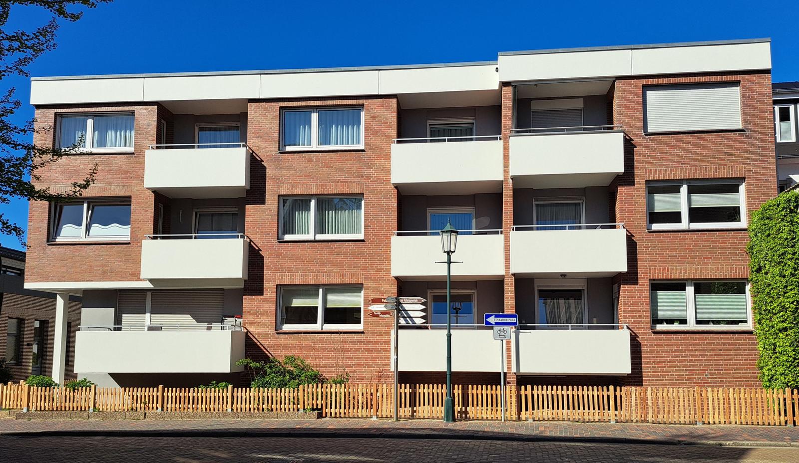Fassade eines Mehrfamilienhauses mit Balkonen und Fenstern unter blauem Himmel.