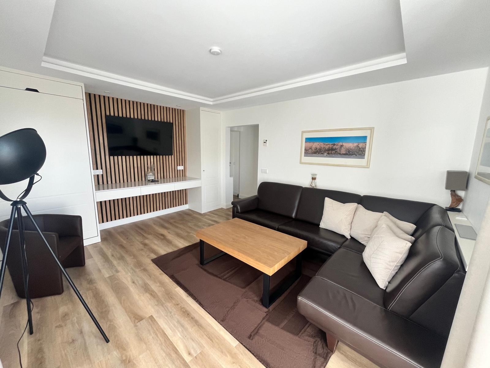 Wohnzimmer mit Sofa, Couchtisch und Fernseher an Holzwand.