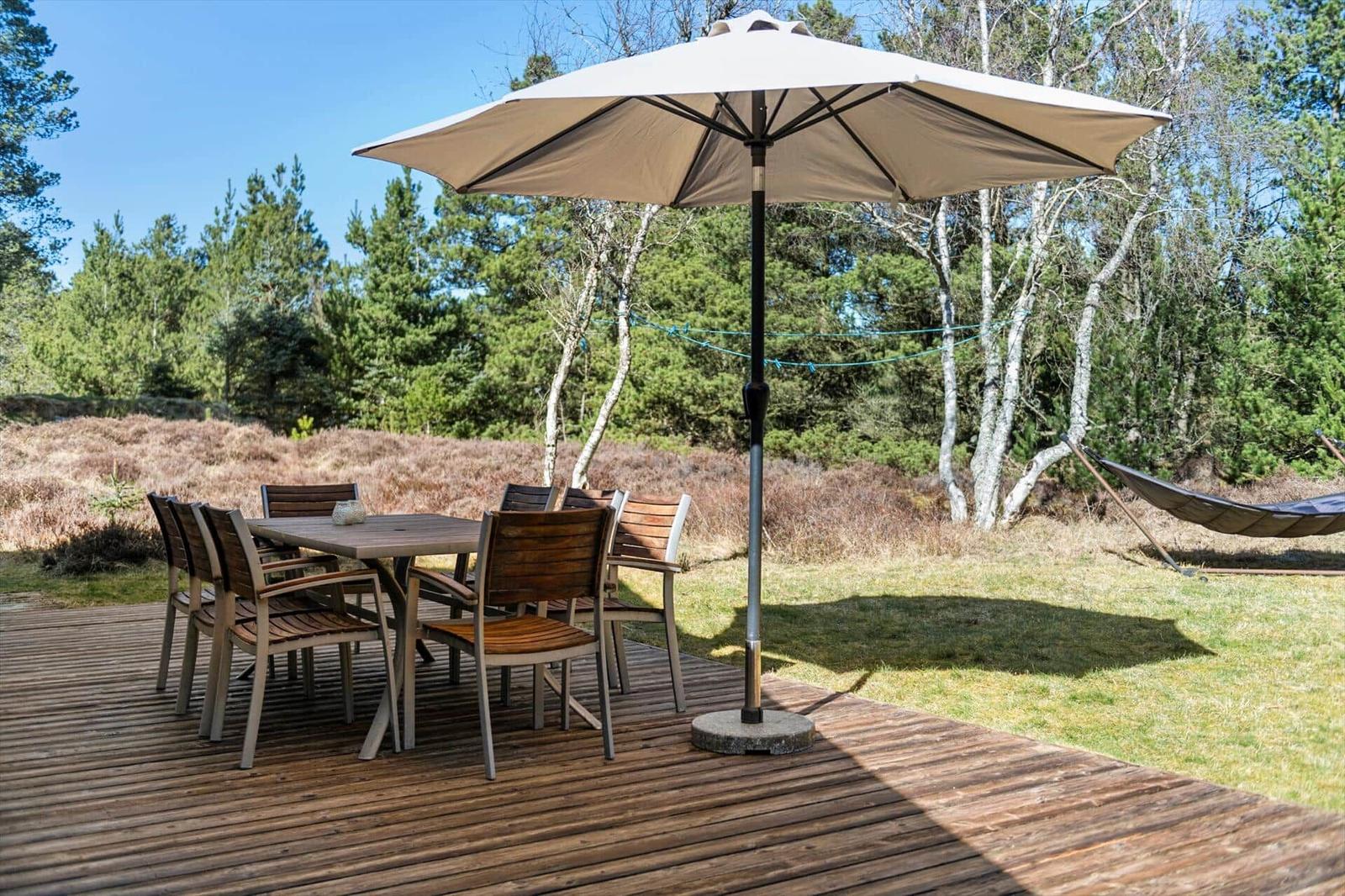 Holztisch mit Stühlen unter einem Sonnenschirm auf einer Terrasse im Wald.