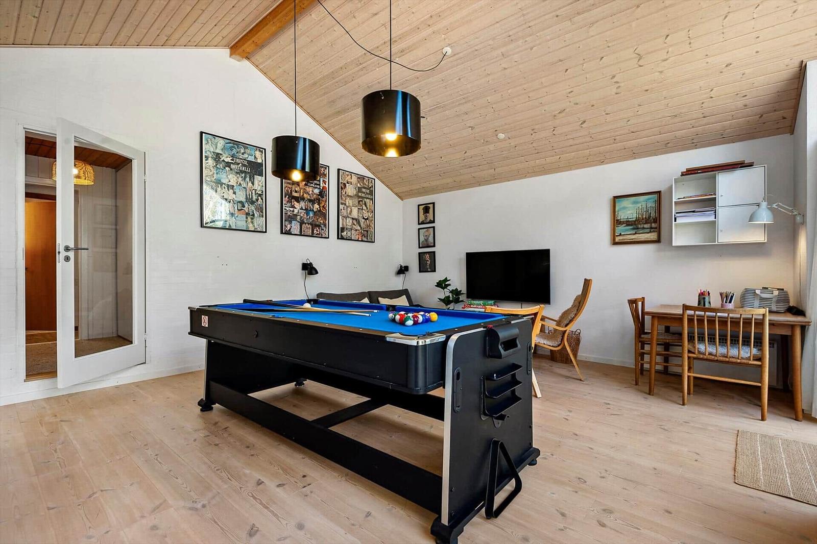Raum mit Billardtisch, TV, Schreibtisch und Holzdecke.