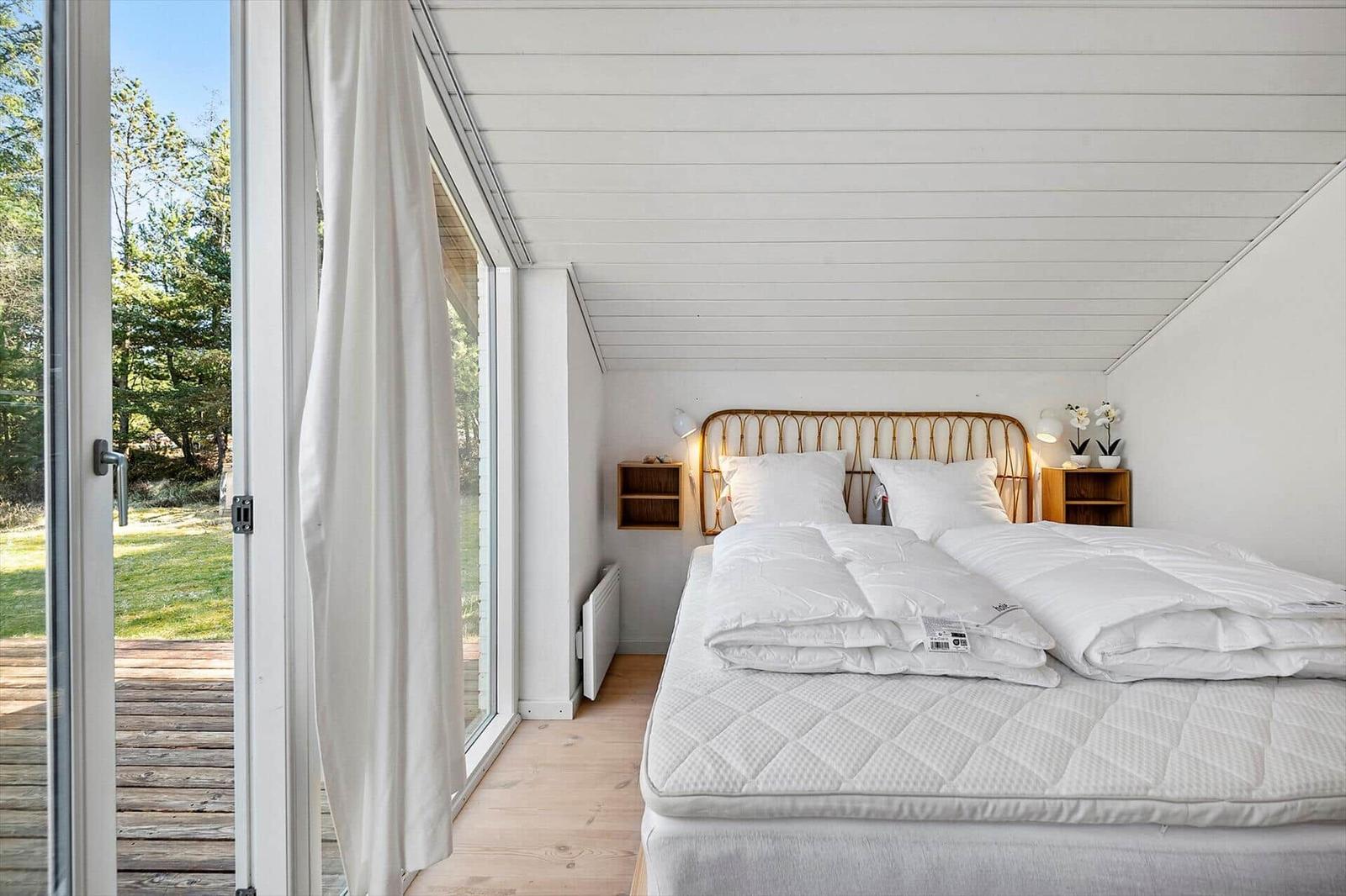 Schlafzimmer mit Doppelbett, Holzdecke und großem Fenster zur Terrasse.