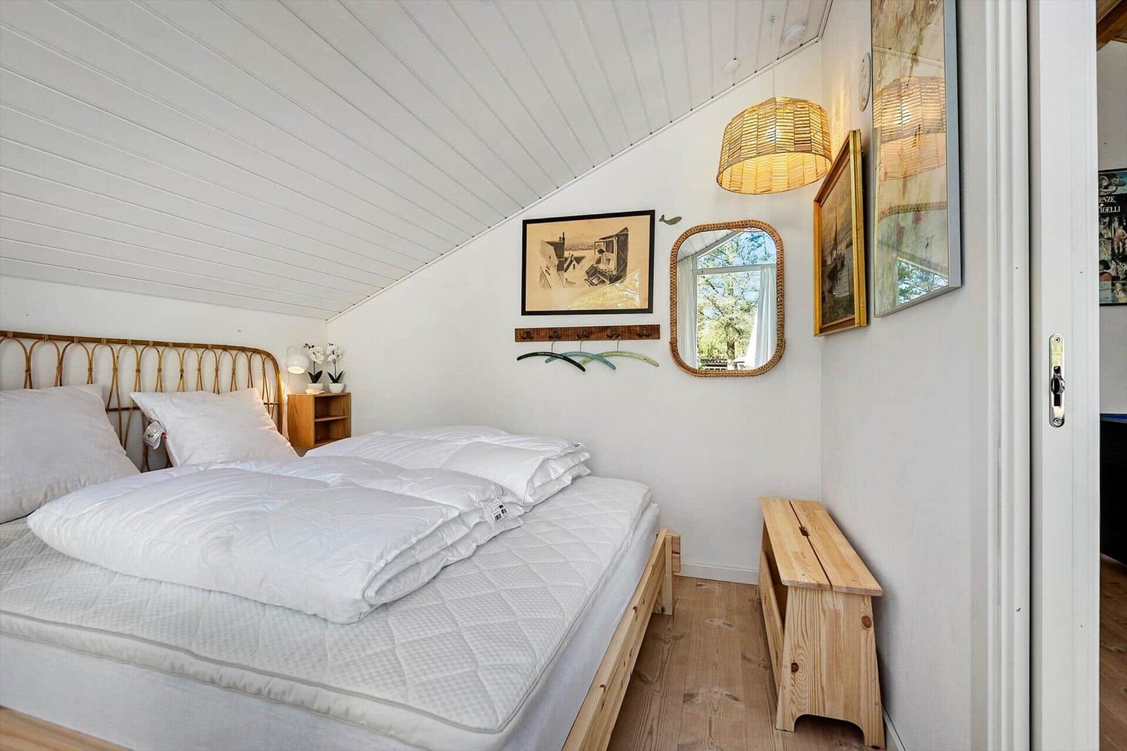 Schlafzimmer mit Doppelbett, Holzboden und Wandbildern. Decke mit weißen Holzdielen.