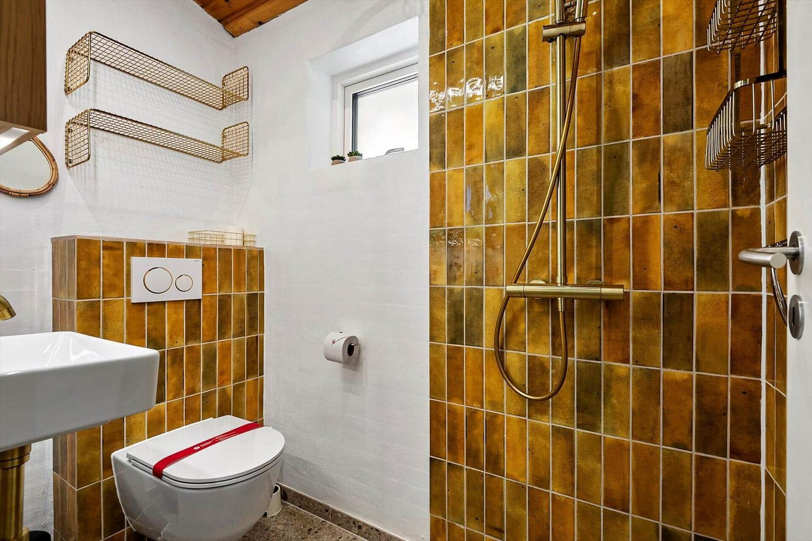 Bad mit Dusche, Toilette und Waschbecken. Wände mit goldenen Fliesen und Metallregalen.