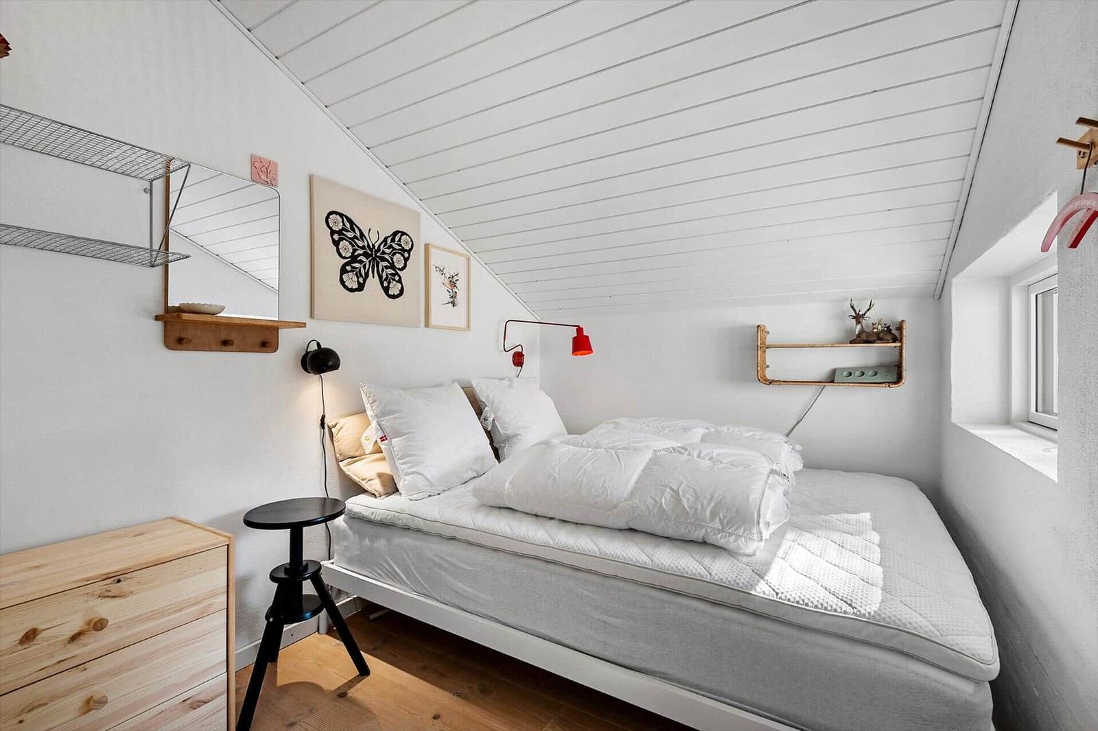 Schlafzimmer mit Bett, Wandregalen und Fenster unter schrägem Dach.