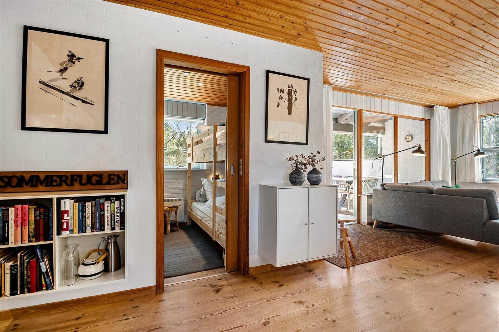 Wohnbereich mit Sofa, Bücherregal und Blick in Schlafzimmer mit Doppelstockbett.