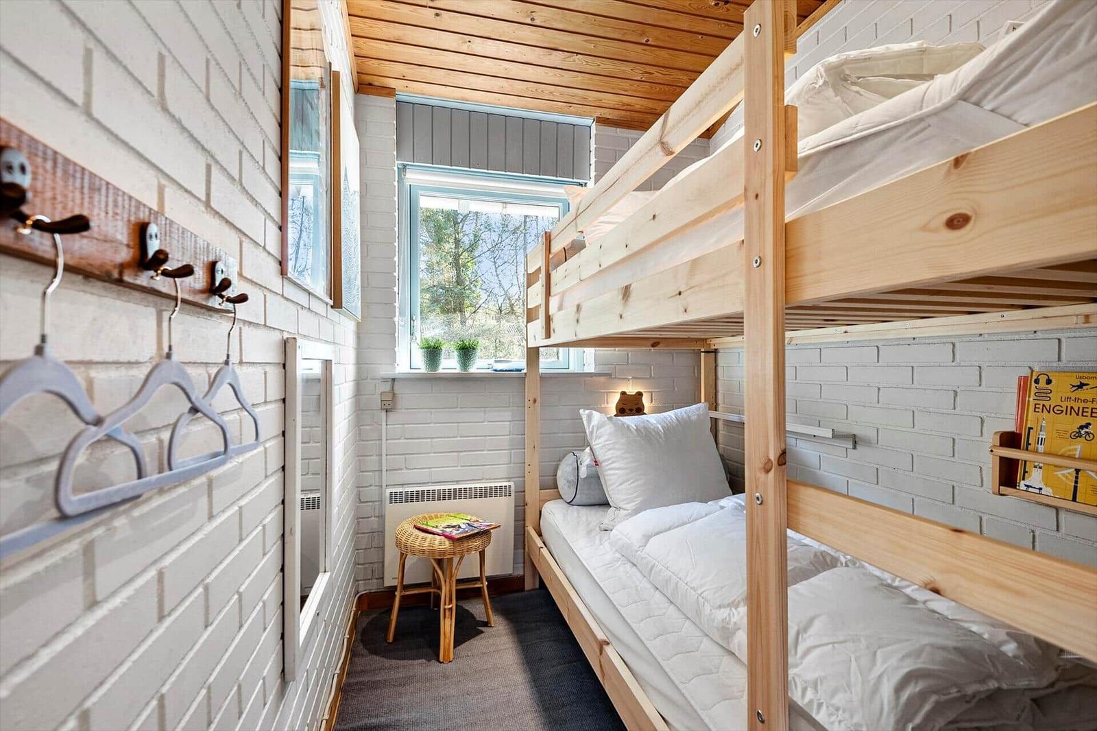 Zimmer mit Holz-Etagenbett, weißer Ziegelwand und Fenster mit Pflanzen.