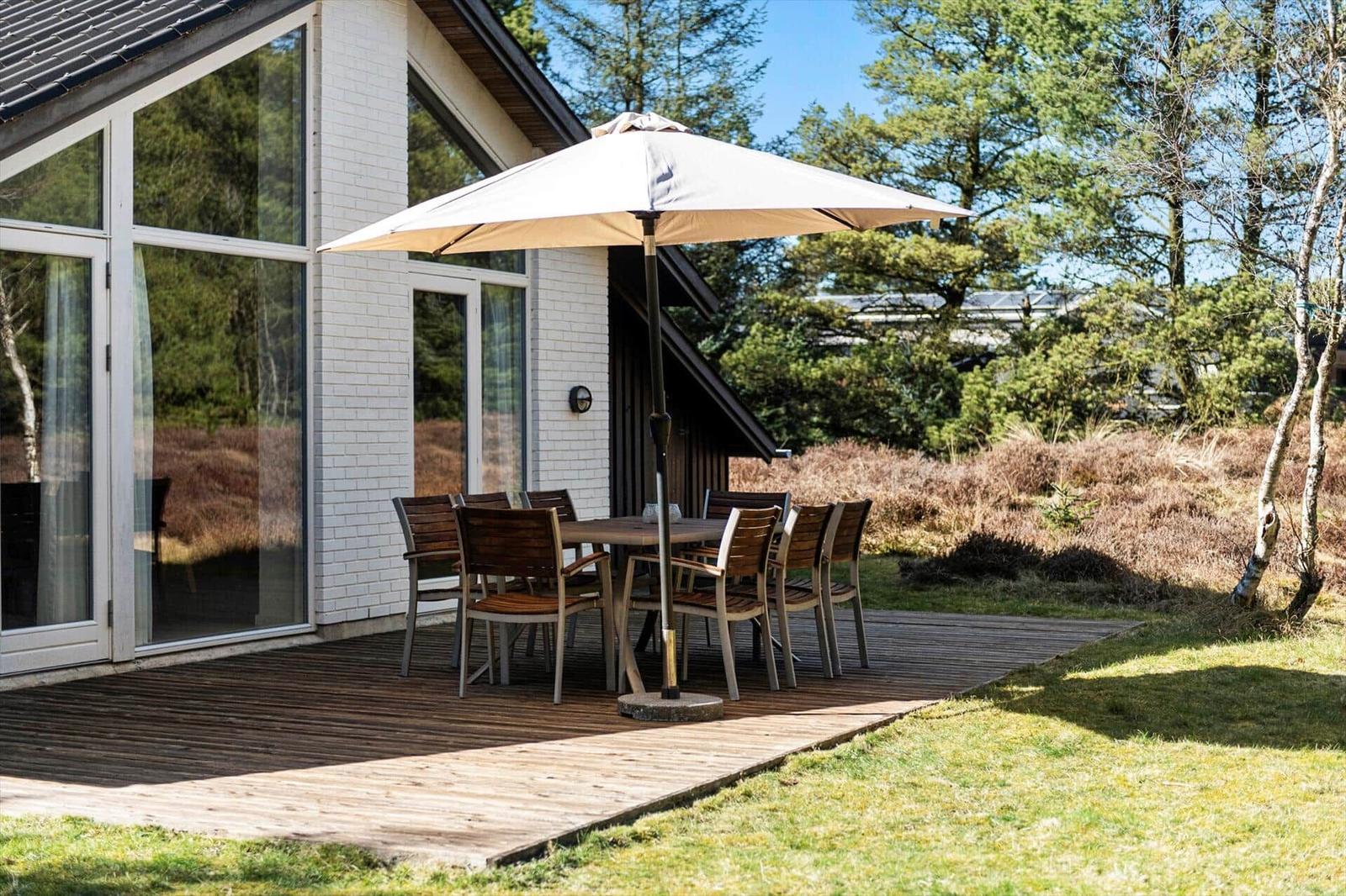 Terrasse mit Tisch, Stühlen und Sonnenschirm neben modernem Haus.