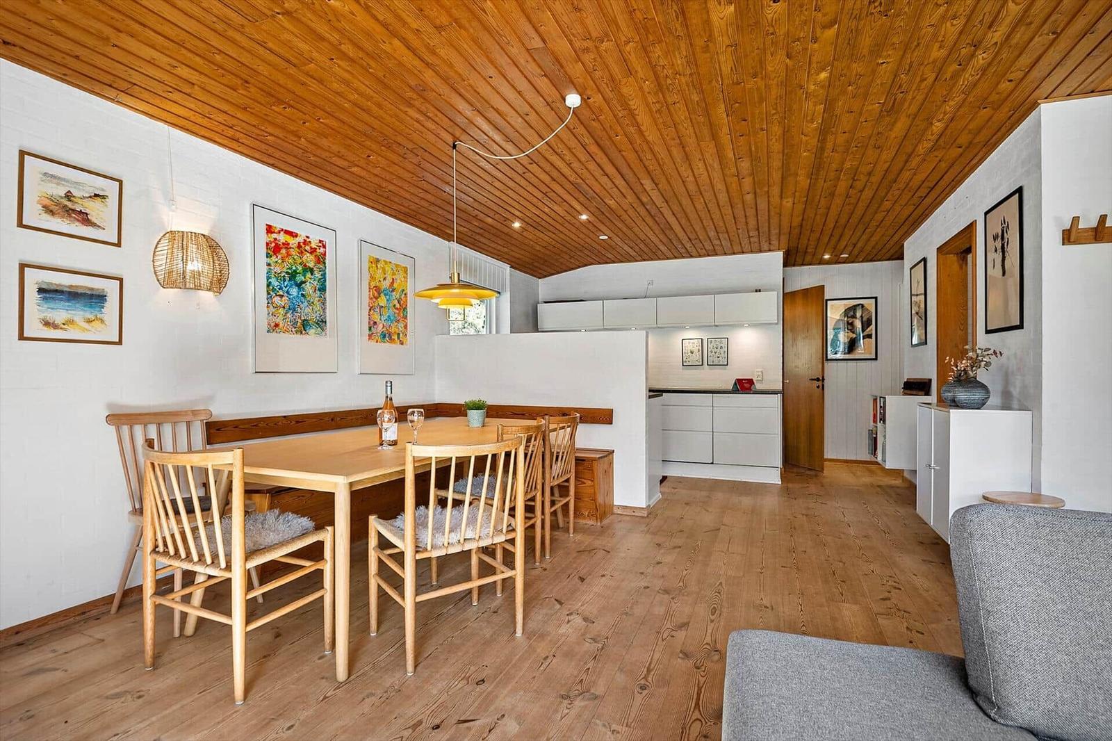 Essbereich mit Holztisch, Stühlen und Küchenbereich im Hintergrund.