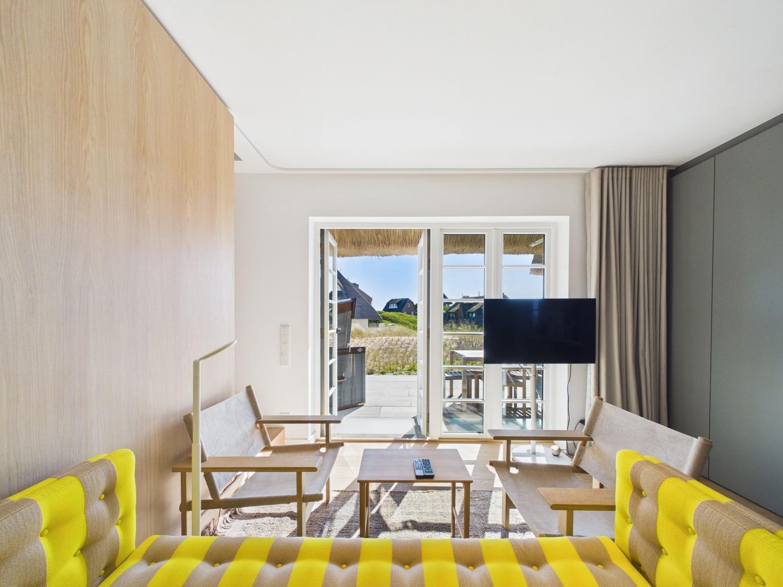 Wohnzimmer mit gelbem Sofa, Fernseher und Terrasse mit Blick.