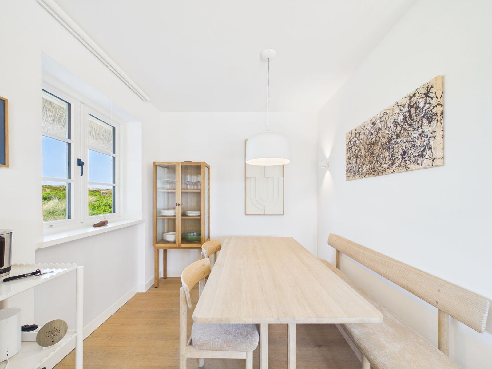 Esszimmer mit Holztisch, Bänken und Glasvitrine. Fenster mit Blick auf Grün.