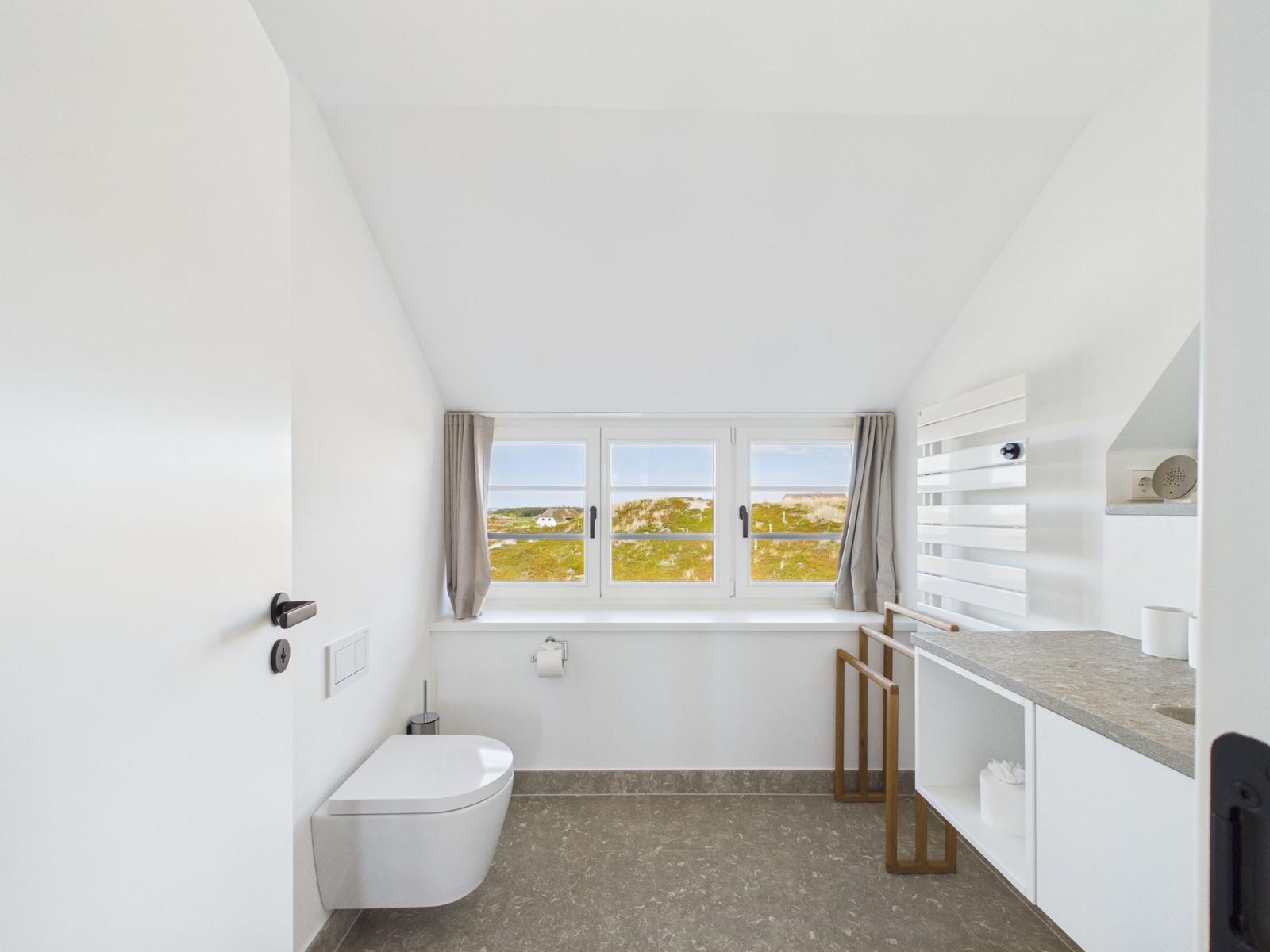 Badezimmer mit Duschbereich und Fensterblick auf die Landschaft.