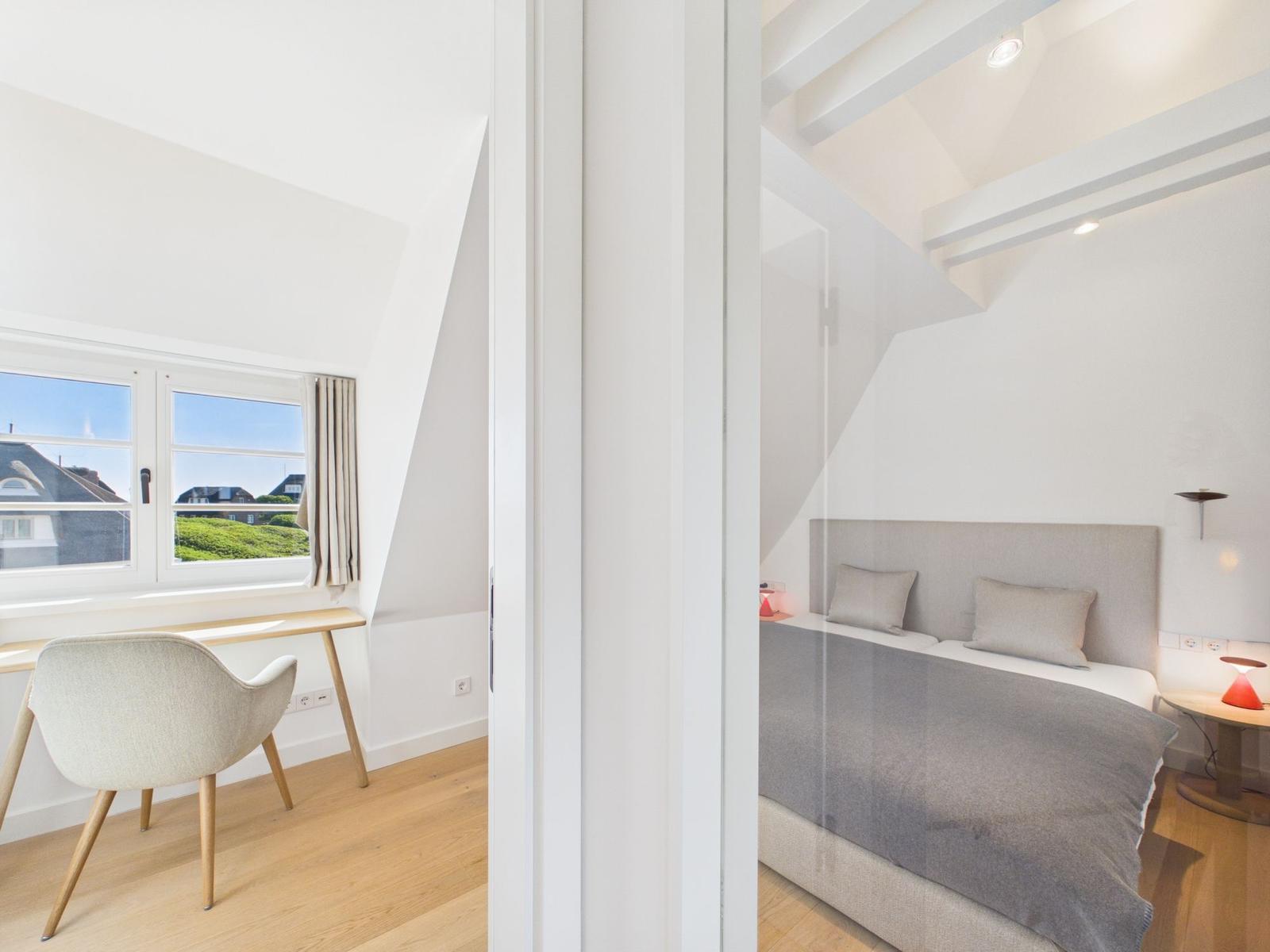 Schlafzimmer mit Bett und Schreibtisch. Blick aus dem Fenster auf Grünflächen.