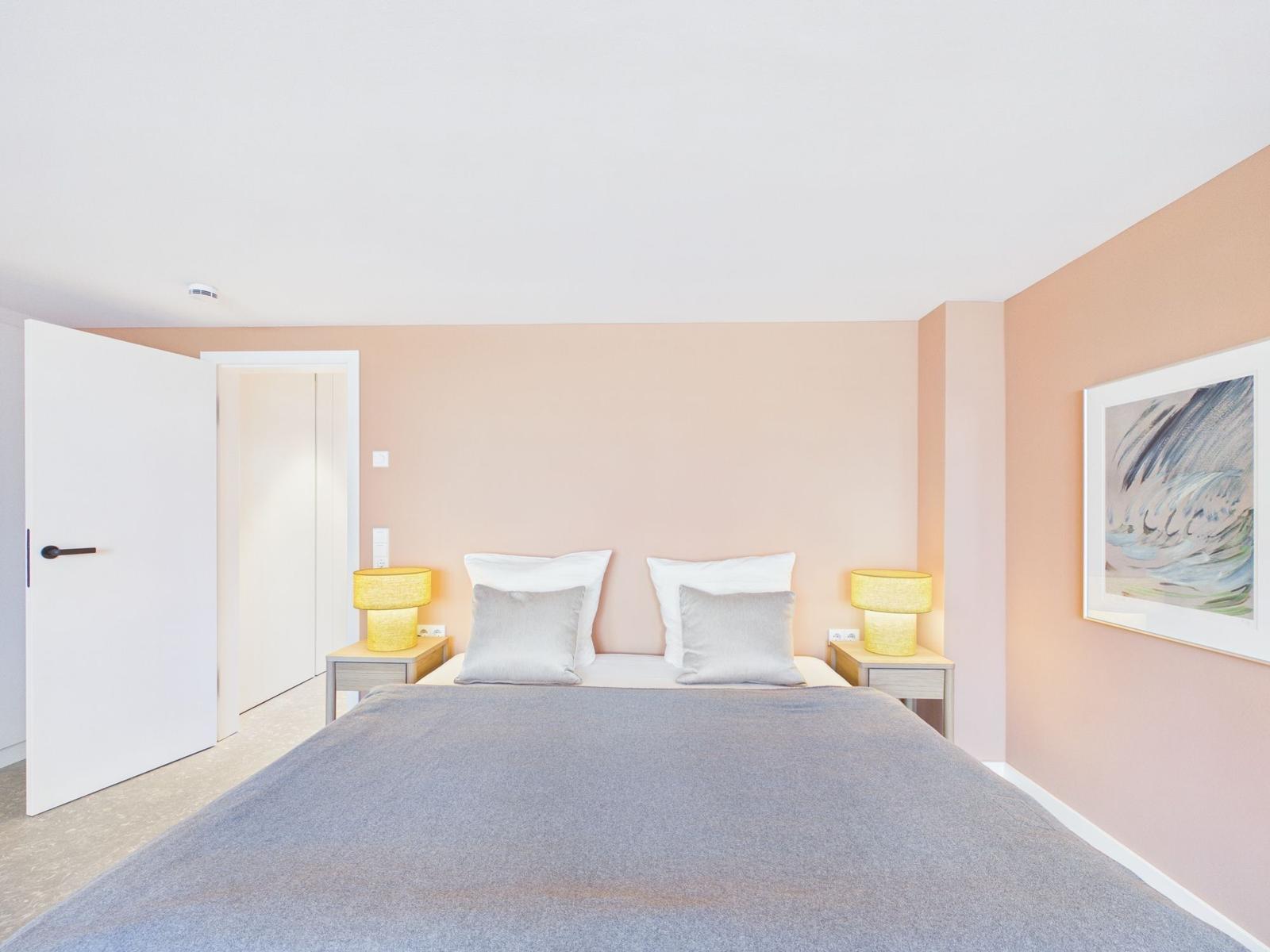 Schlafzimmer mit Bett, zwei Nachttischen und Lampen an den Wänden.