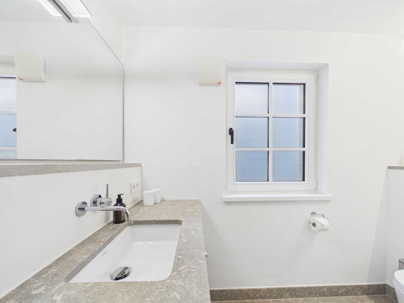 Badezimmer mit Waschbecken, Spiegel und Fenster