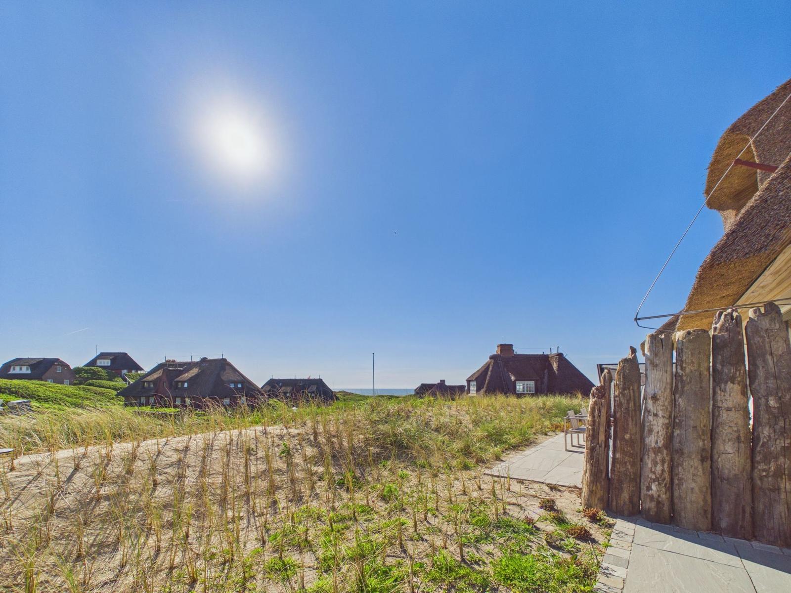 Dorfhäuser mit Strohdächern am Strand unter blauem Himmel.
