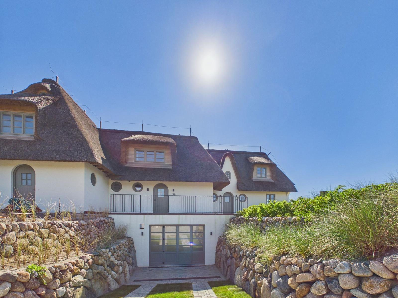 Haus mit Strohdach, Steinmauern und Balkon unter blauem Himmel.