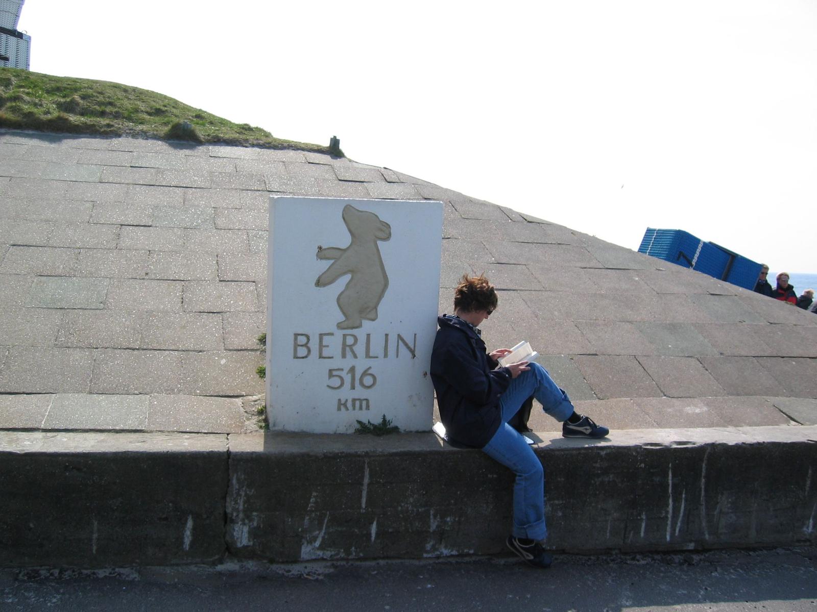 A person sits next to a sign reading Berlin 516 km.