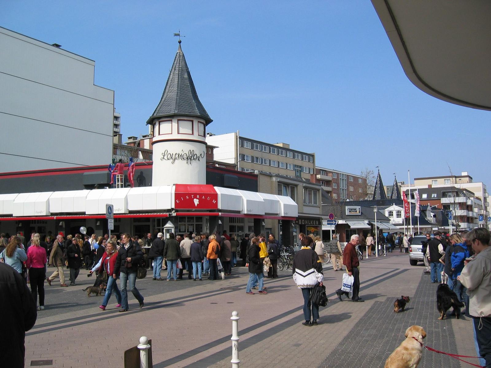 Market square with people and a tower building with an ice cream shop.