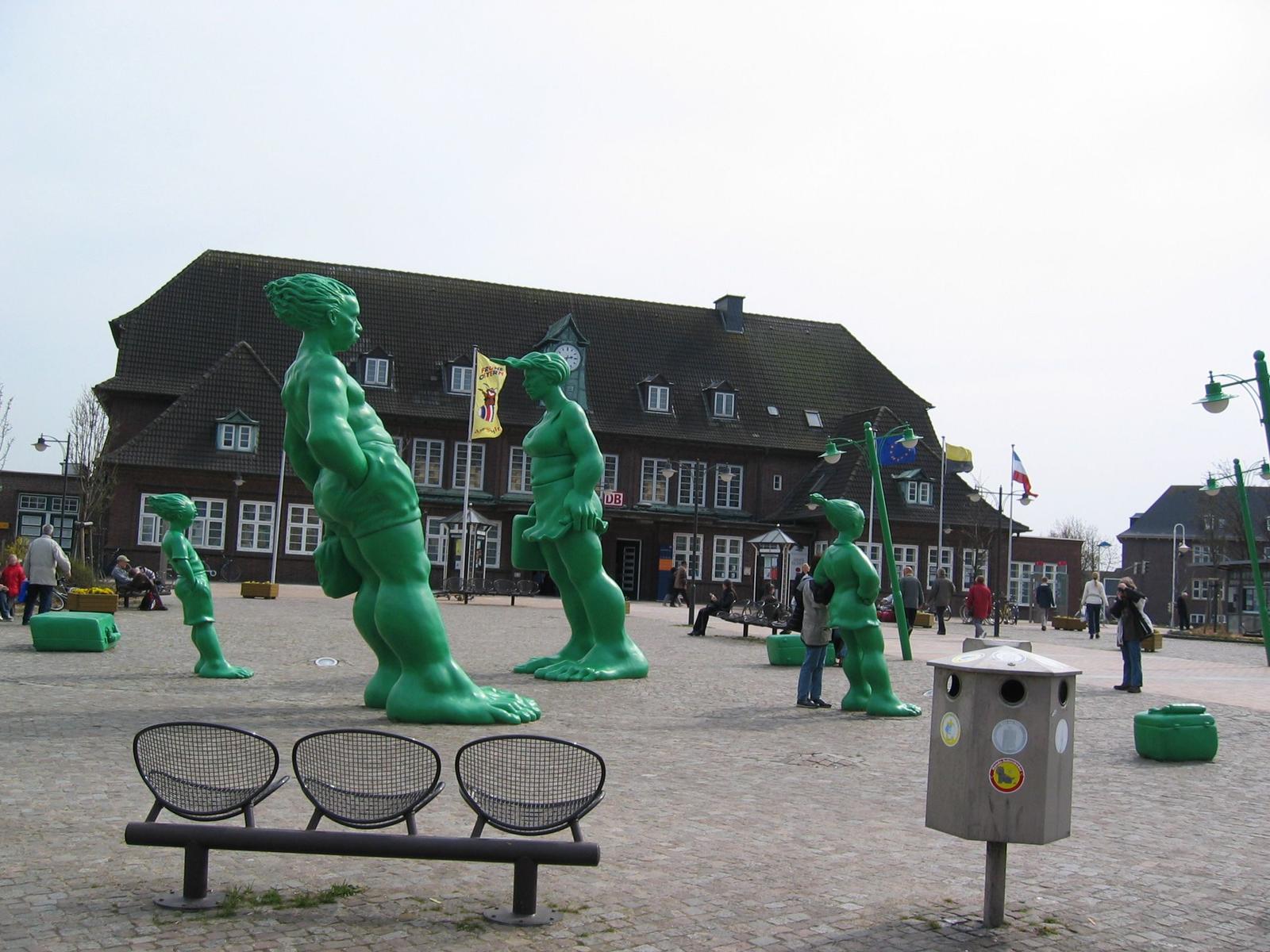 Large green sculptures in the station square with seating and flags.