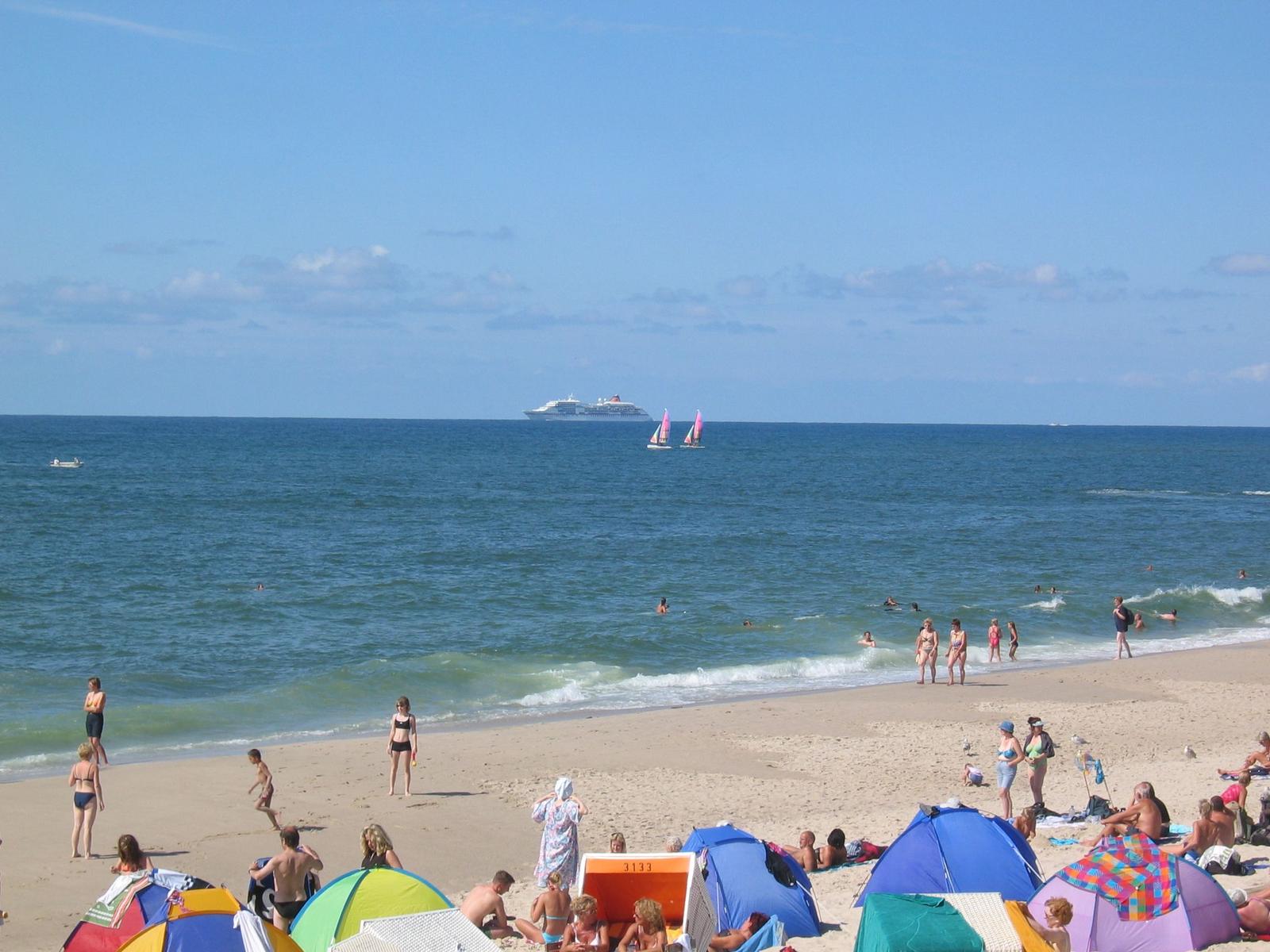 Beach with colorful tents, people, and boats in the sea.