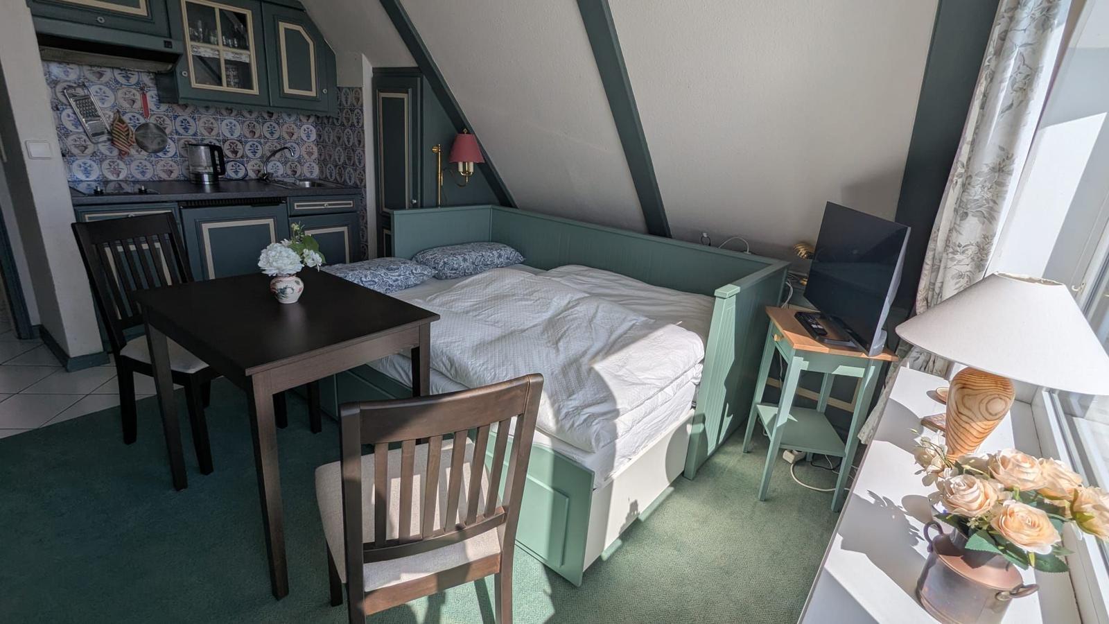 Bedroom with bed, dining table, and kitchen area under sloped ceilings.