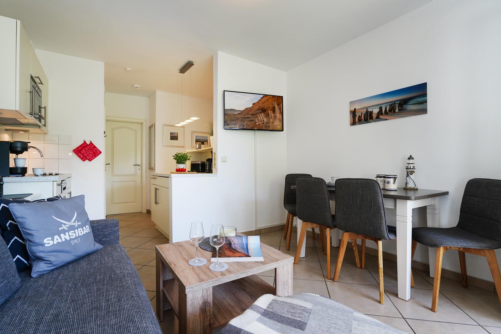 Wohnzimmer mit Küchenbereich, Esstisch und Fernseher an der Wand.