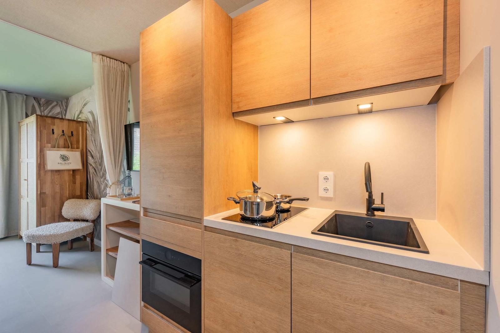 Küche mit Holzschränken, Spüle und Herd. Im Hintergrund ist ein Schrank und ein Stuhl sichtbar.