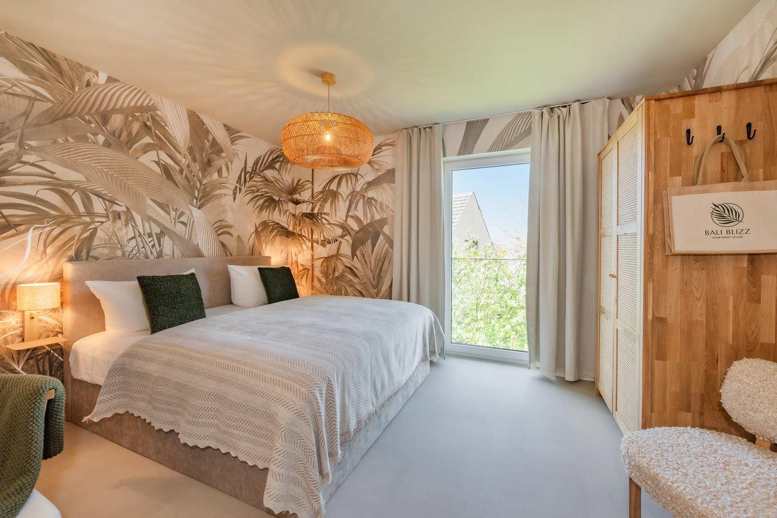 Schlafzimmer mit Bett, Wandtapete und Fenster. Holzgarderobe und Hängeschild.