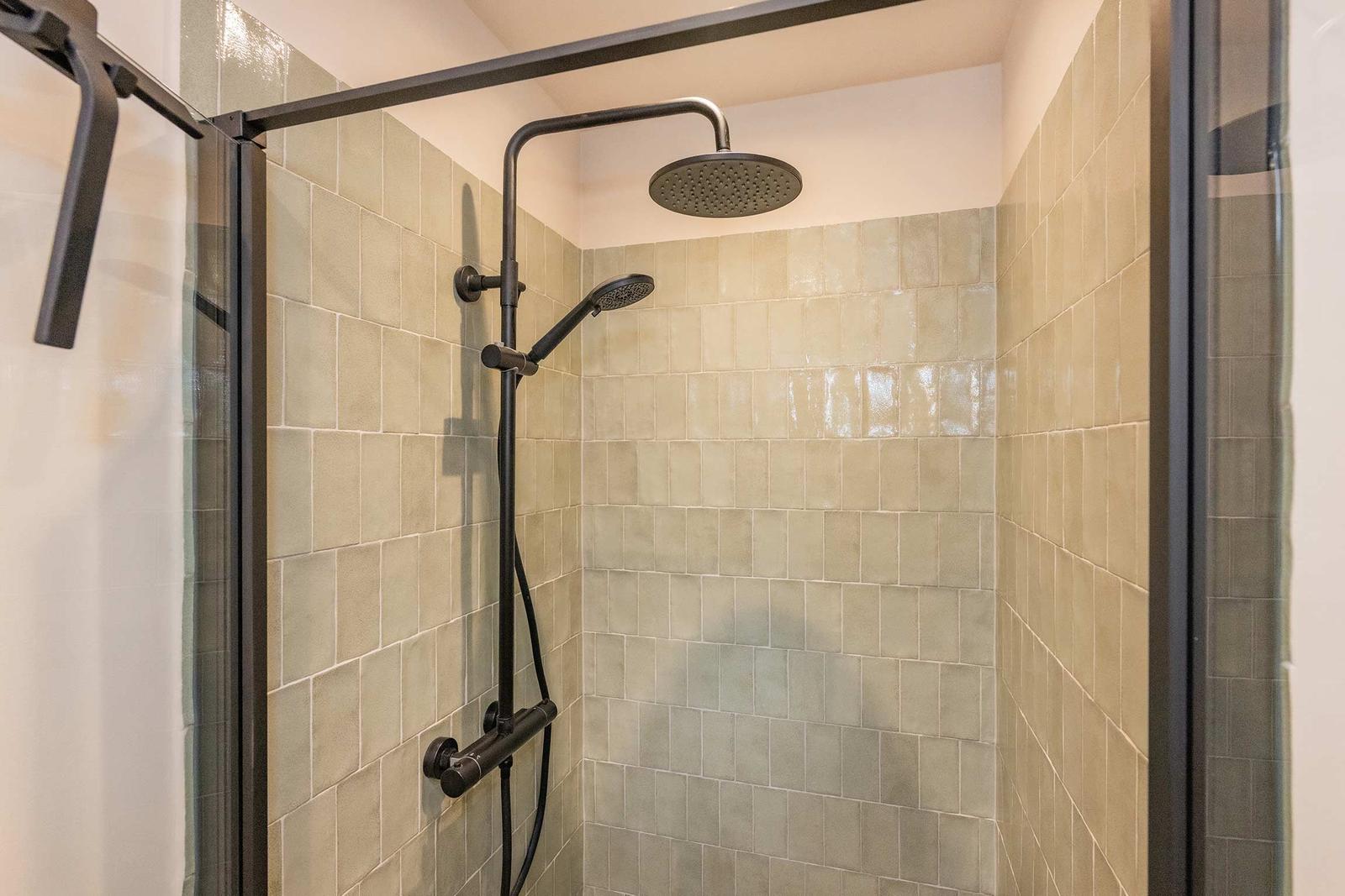 Dusche mit Glaswand und schwarzen Armaturen an beigefarbenen Fliesen