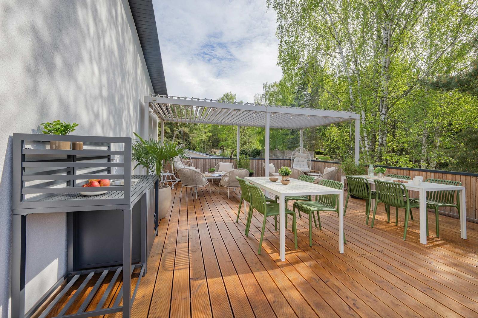 Terrasse mit Holzboden, weißem Pavillon, grünen Stühlen und Tischen, Pflanzen und Blick in den Wald.