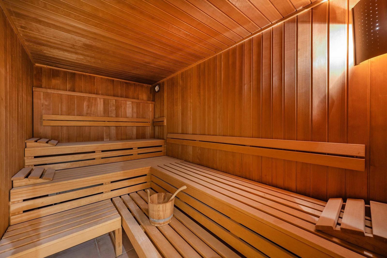 Holzsauna mit Sitzbänken und Eimer. Wände und Decke aus Holz.