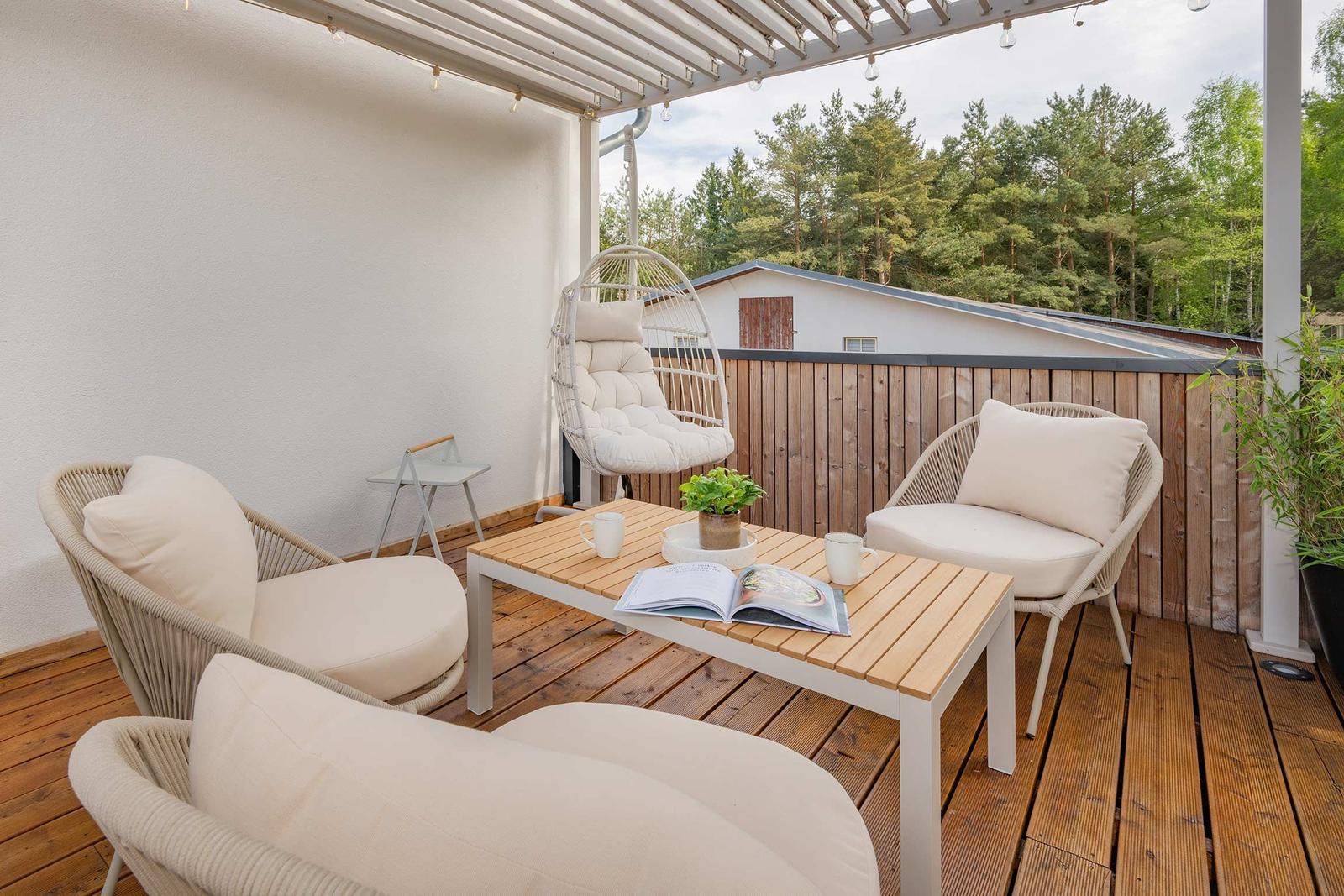 Terrasse mit Sitzgruppe, Tisch und Hängesessel. Holzdecke und Blick auf Wald.