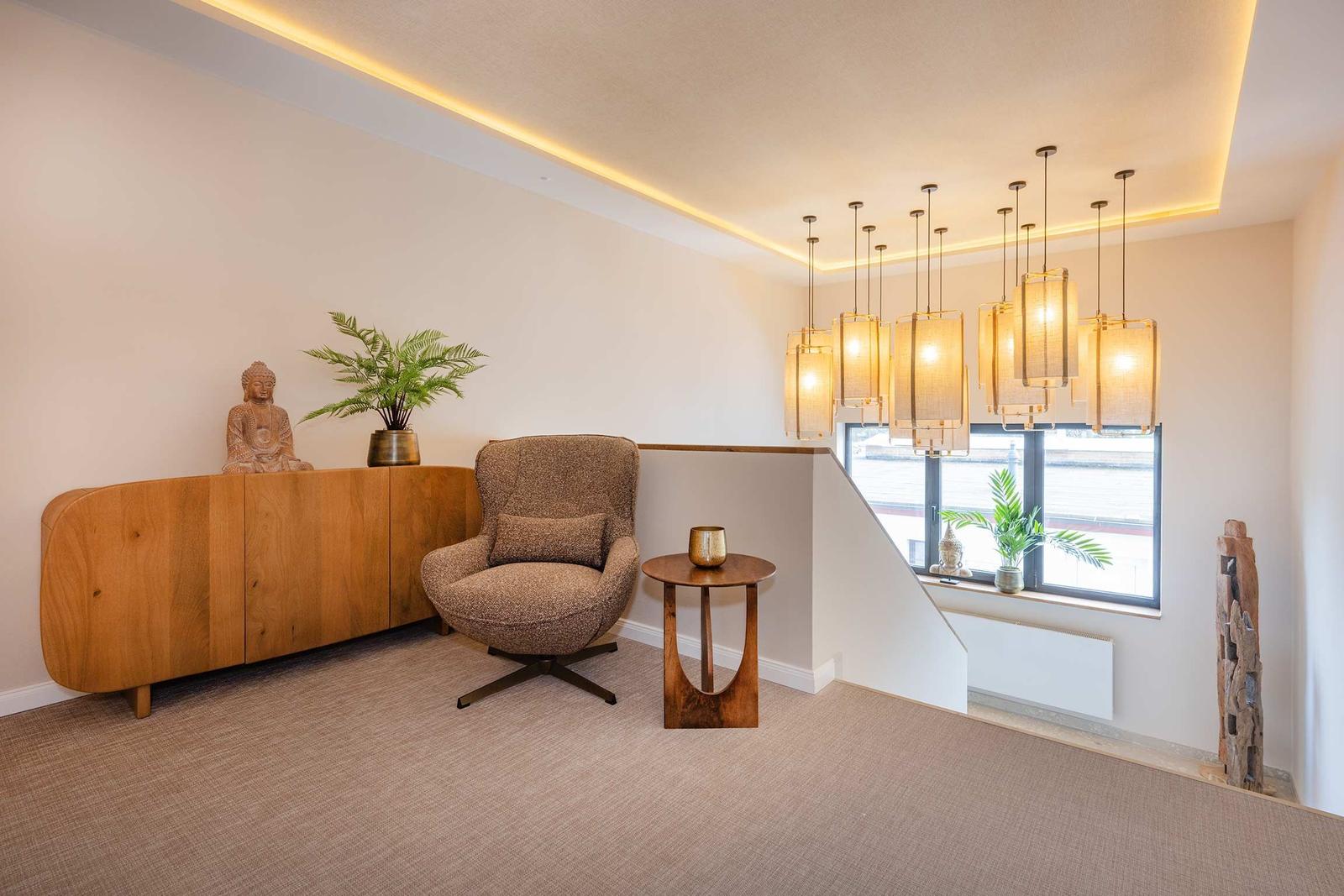 Ein Raum mit Sessel, Sideboard, Pflanzen und hängenden Lampen.