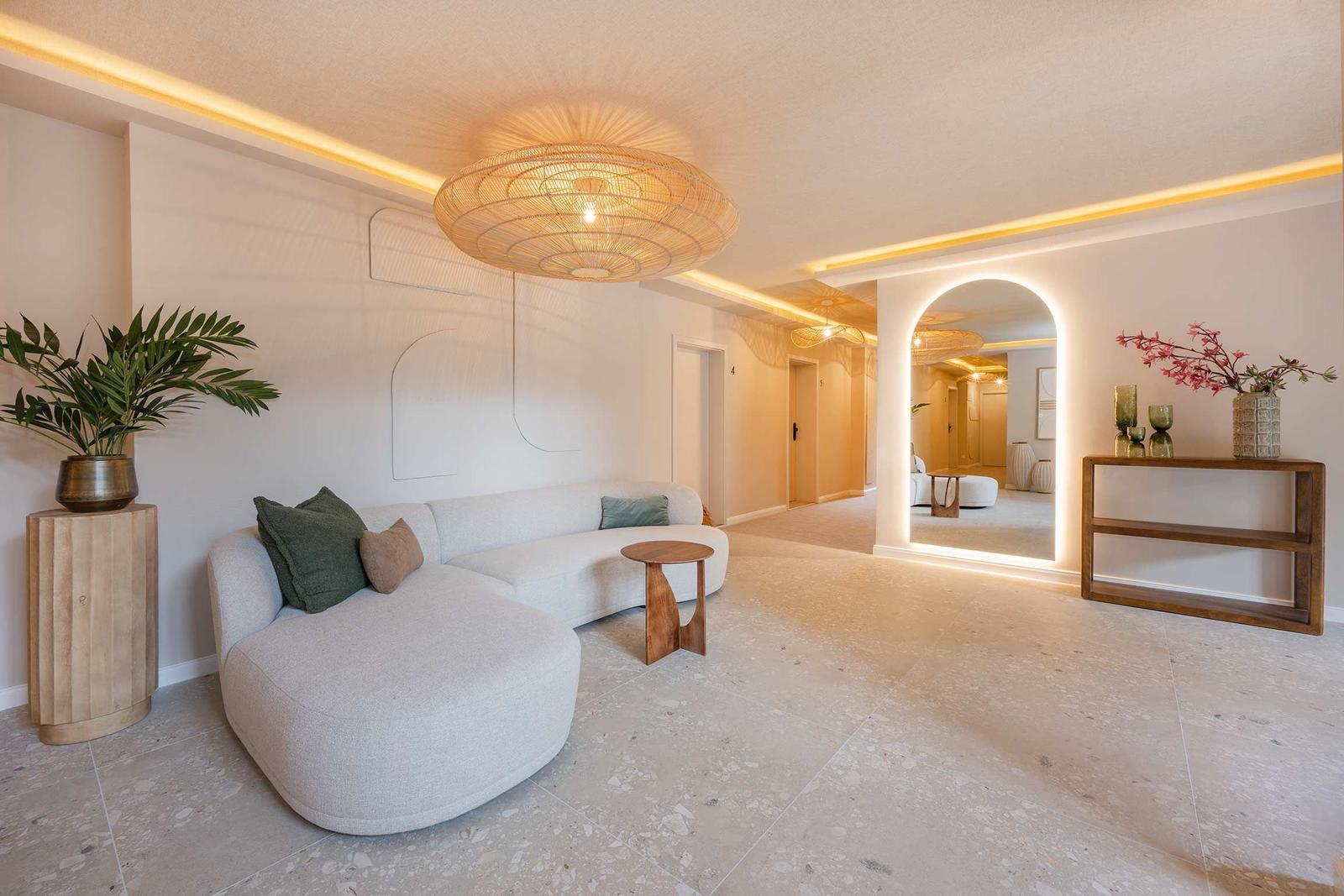 Wohnbereich mit Sofa, Beistelltisch und Pflanzen. Helle Beleuchtung und Terrazzo-Boden.