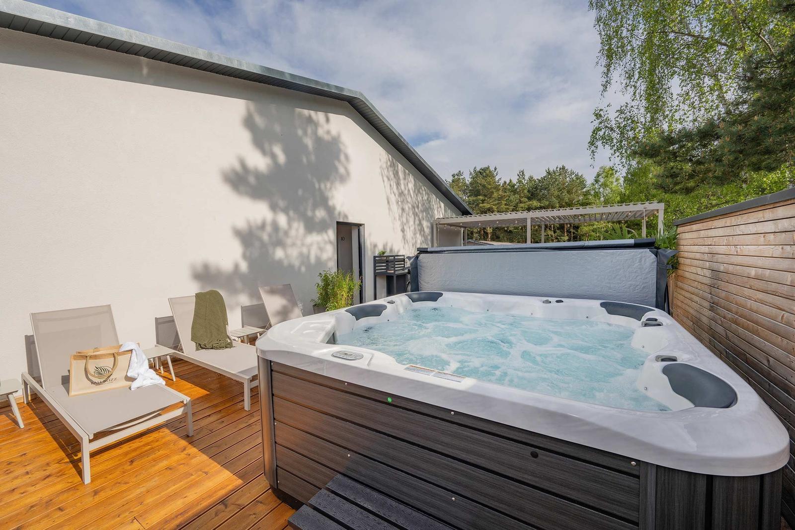 Außenbereich mit Whirlpool, Sonnenliegen und Holzterrasse neben einem Haus.