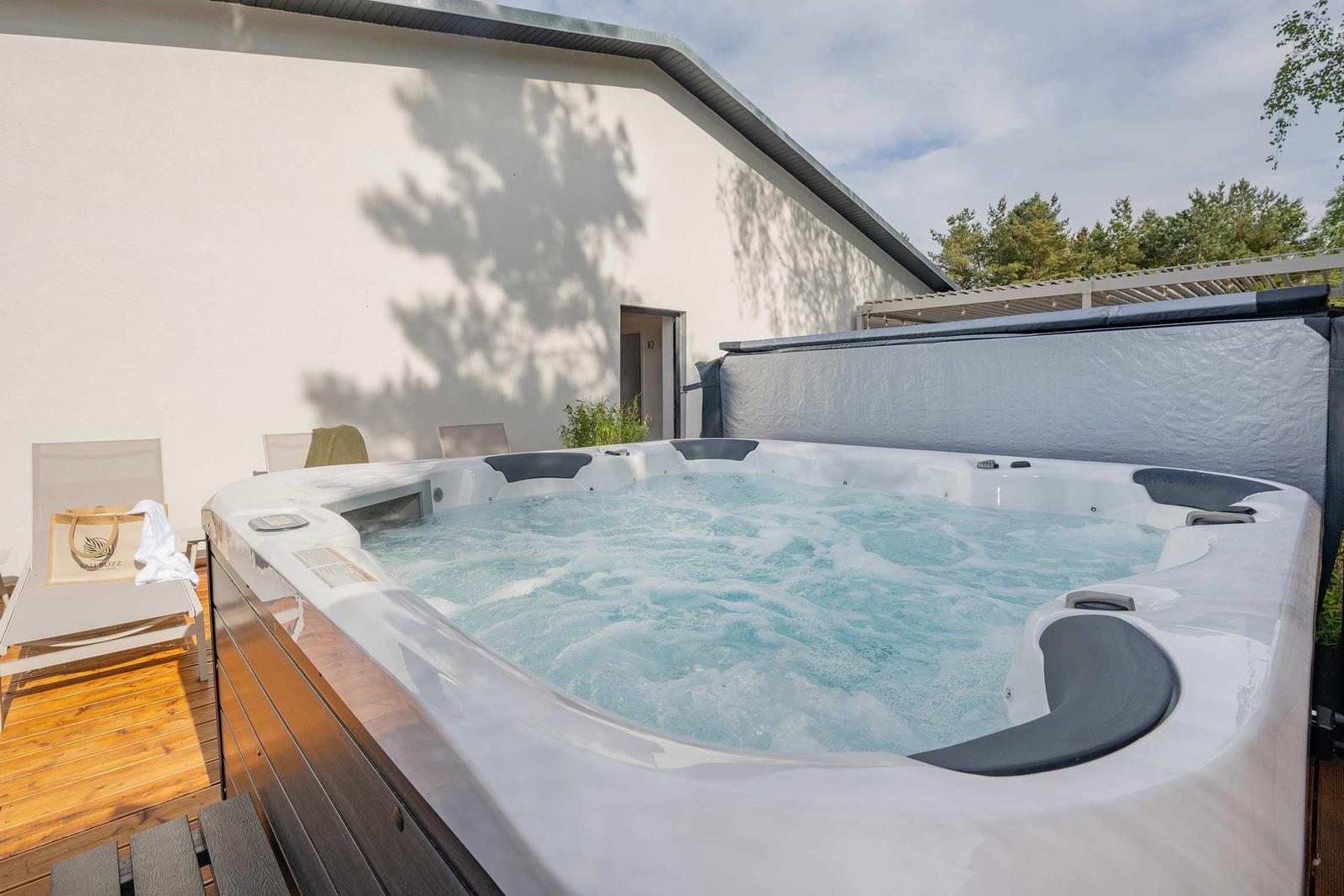Ein Whirlpool mit blauem Wasser auf einer Holterrasse vor einem weißen Gebäude.