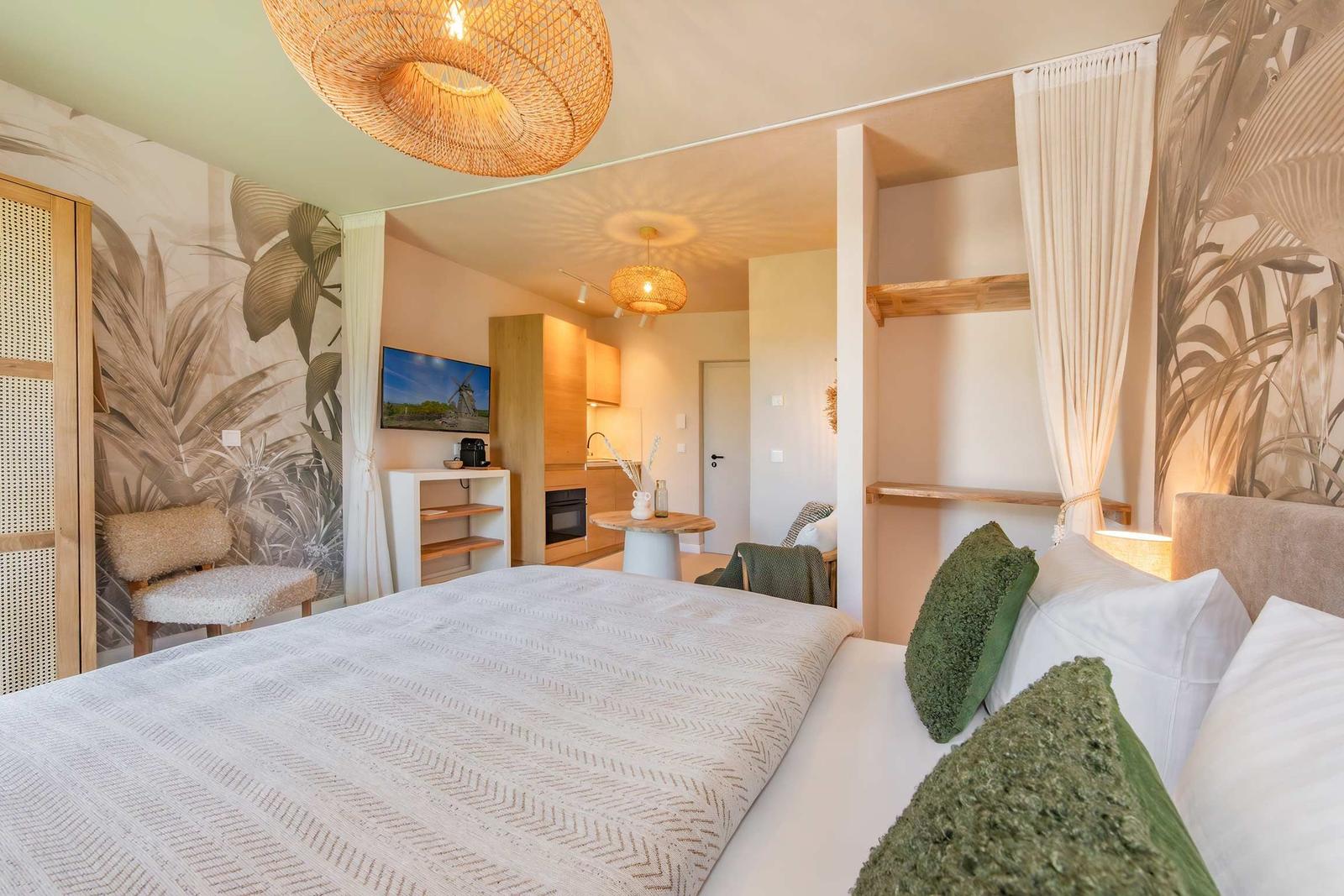 Schlafzimmer mit Bett, Wandtapete und Blick in Wohnbereich mit Küchenzeile.