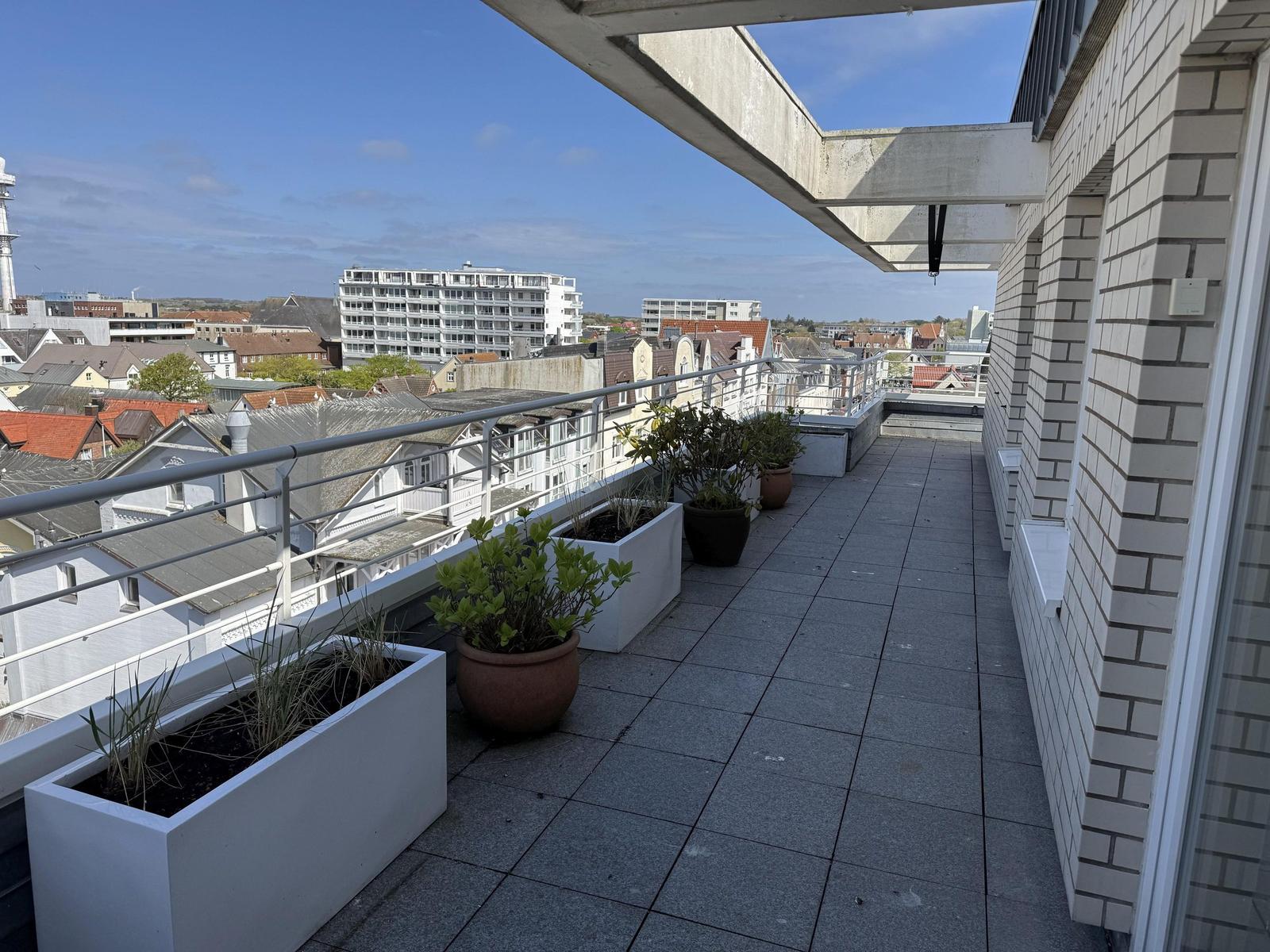 Terrace with plants and city view. Grey tiles and white wall elements.