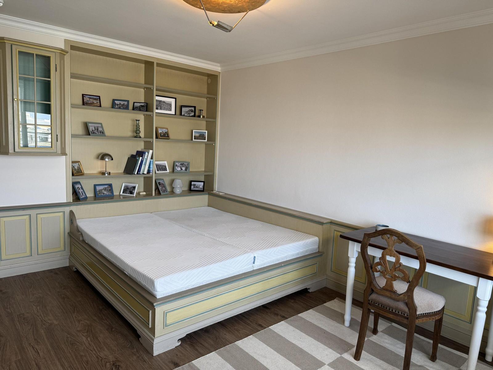 Bedroom with bed, desk, and wall unit with picture frames.