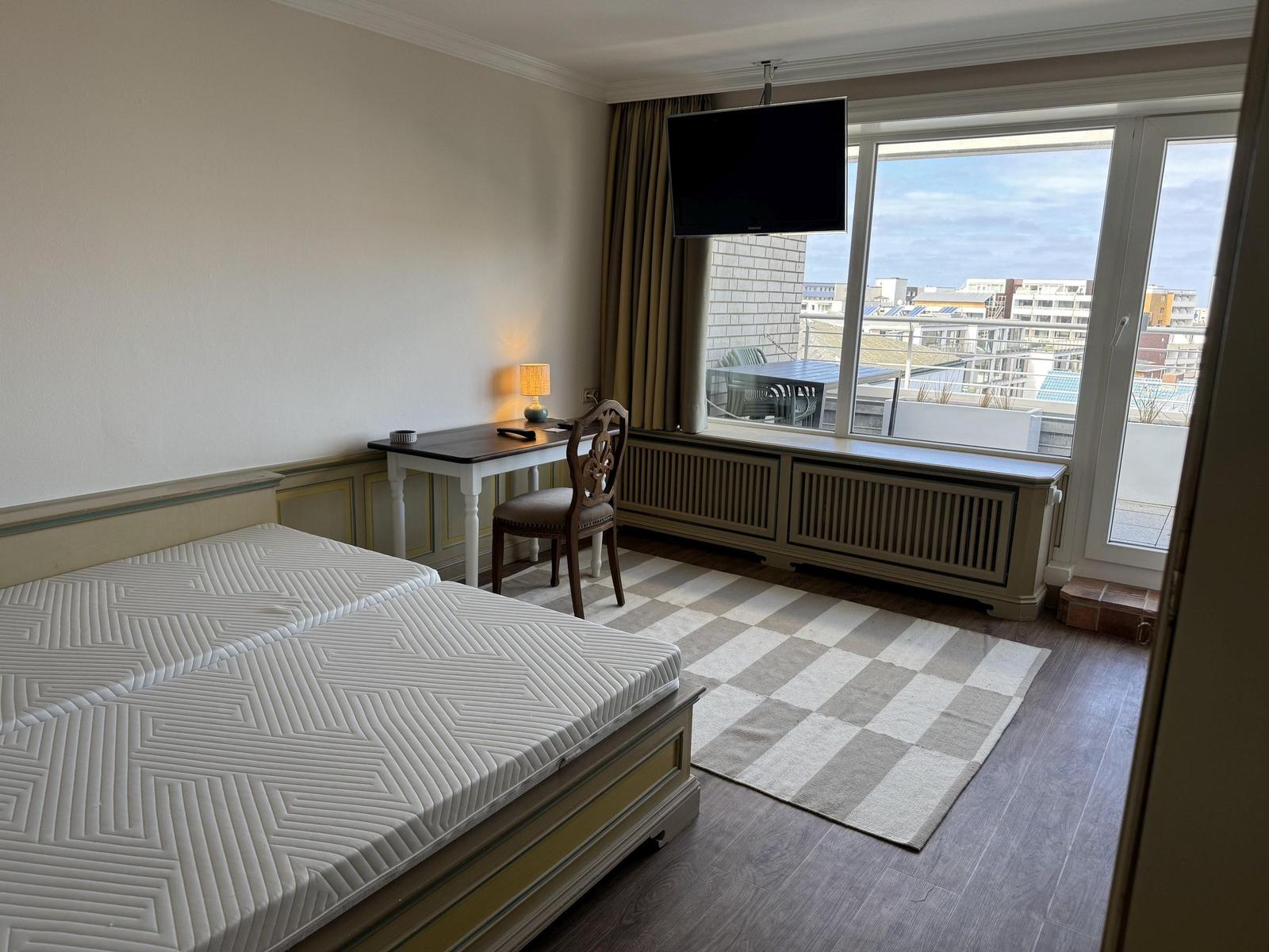 Room with double bed, desk, and balcony view of city