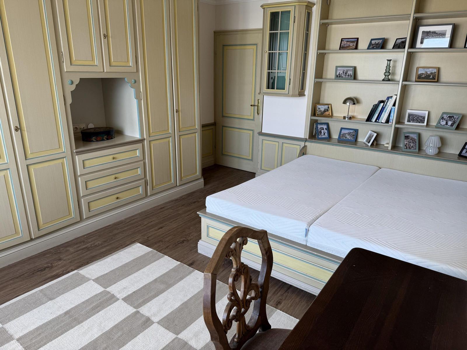 Bedroom with double bed, wardrobe, and bookshelf. Wooden floor and rug.