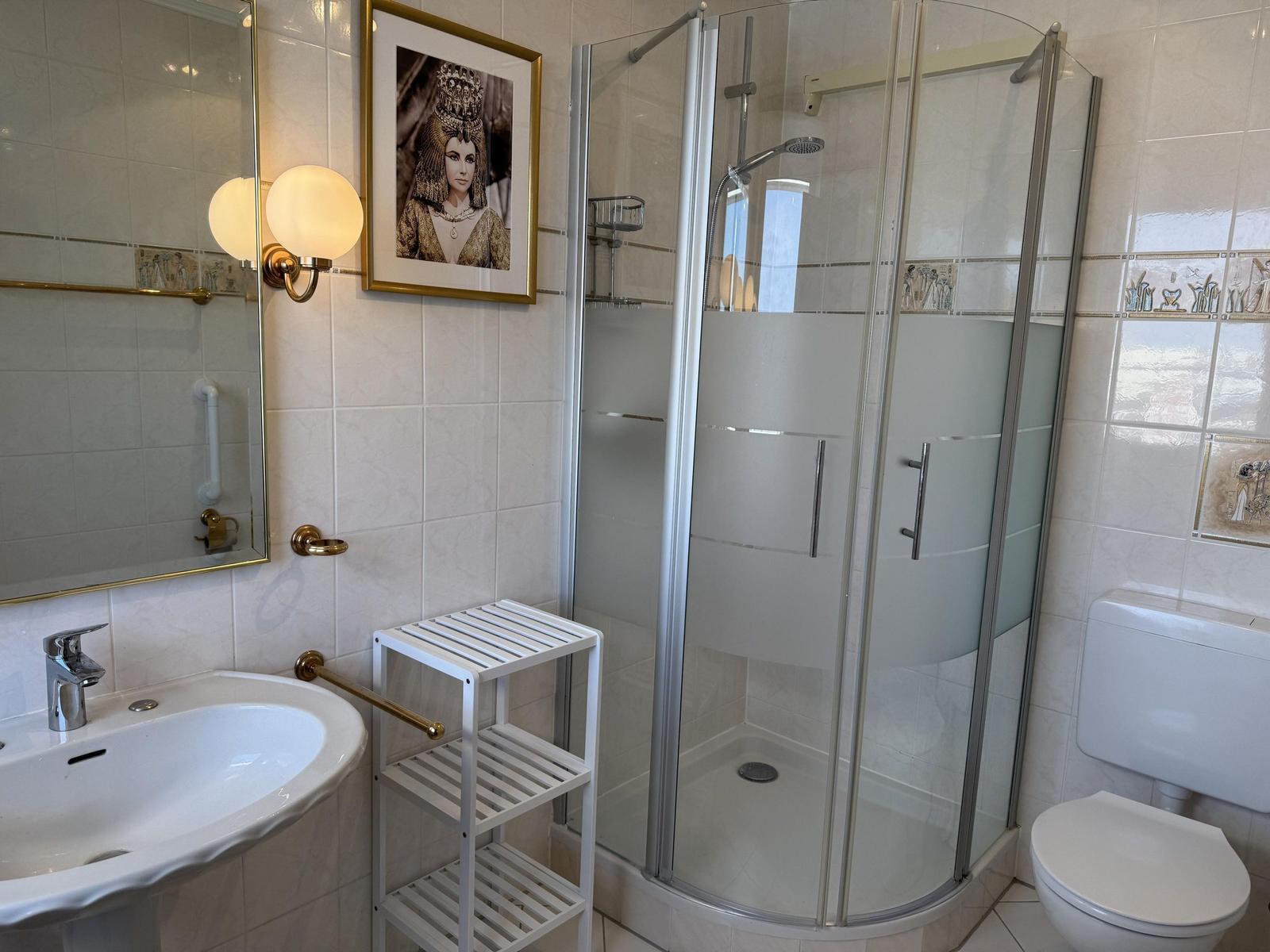 Bathroom with shower, sink, and toilet. Wall picture and mirror are visible.