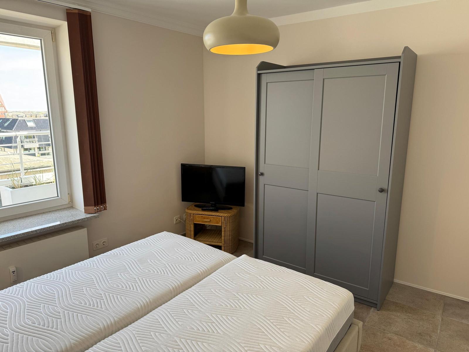Bedroom with double bed, wardrobe, and TV. Window with view of rooftops.
