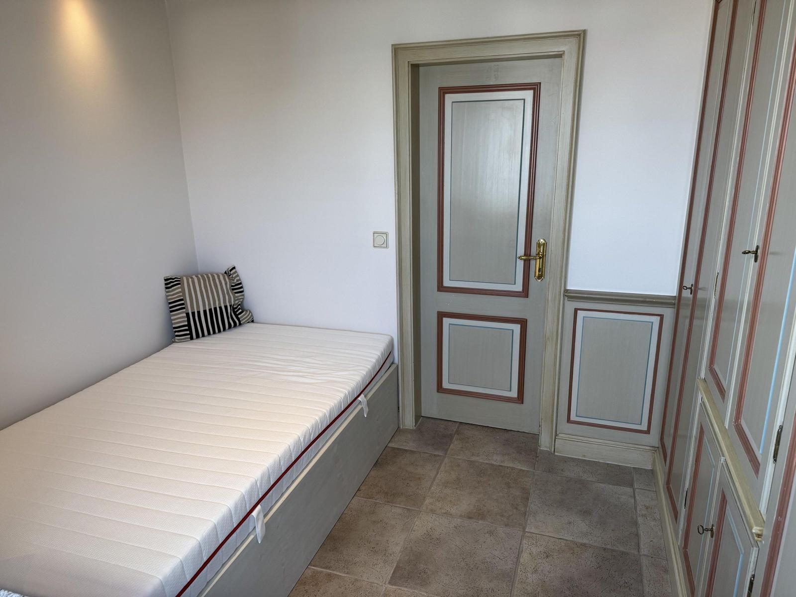 Bedroom with mattress, pillow, and door. Tile floor and wardrobe.