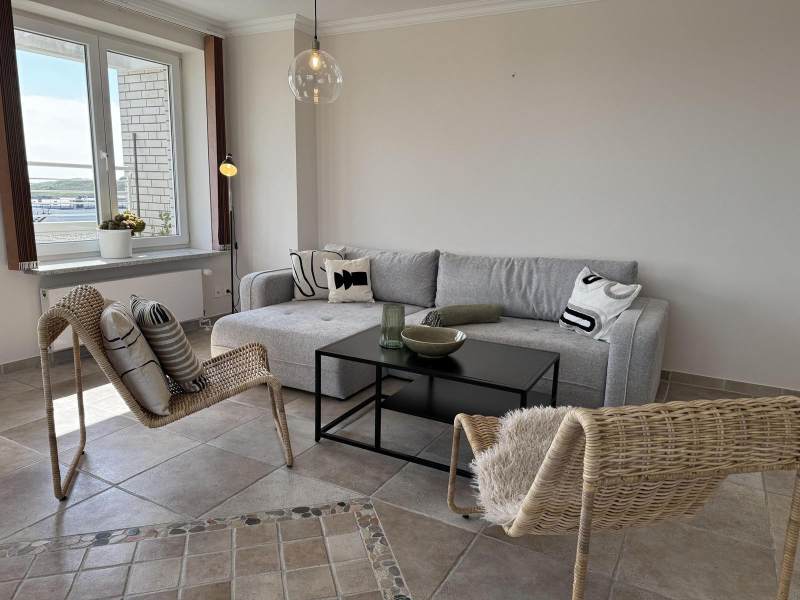 Living room with gray sofa, two rattan chairs, and large window.
