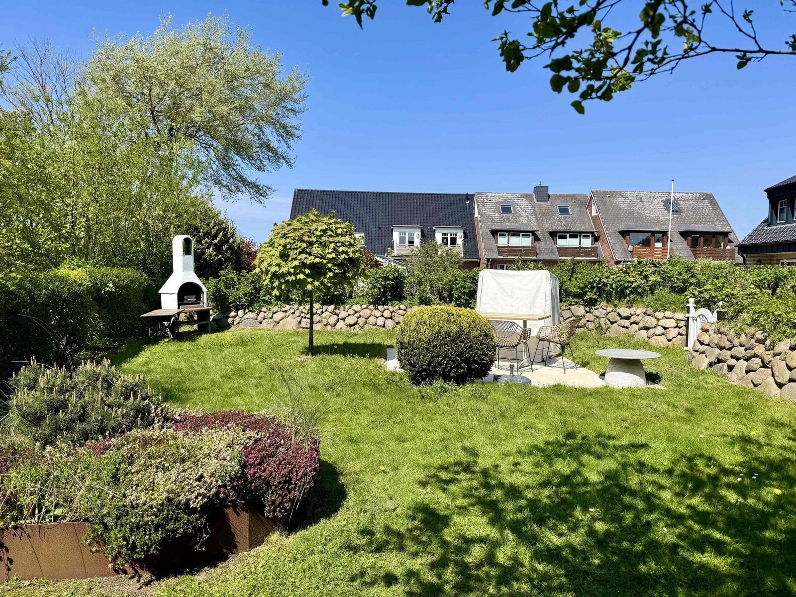Garten mit Grill, Sitzgruppe und Rasenfläche. Im Hintergrund sind Häuser zu sehen.